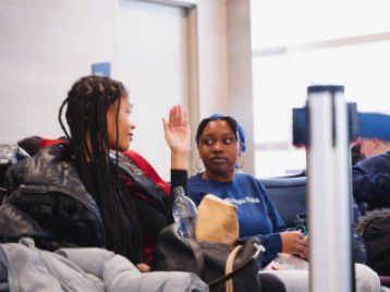 Two UM students talking while sitting at the DTW airport waiting for a flight.